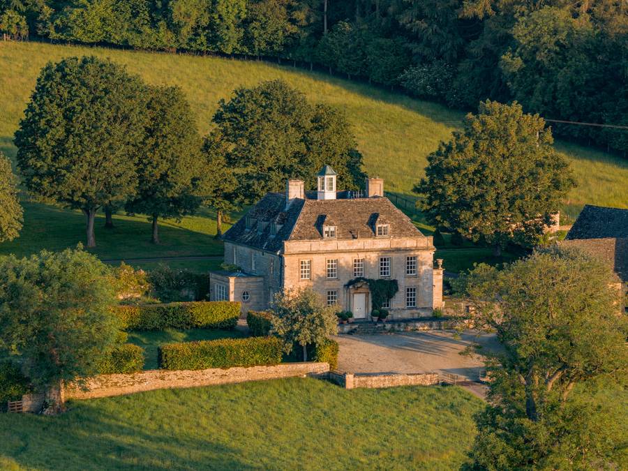 Aerial golden-hour view of a Cotswold manor house among rolling fields